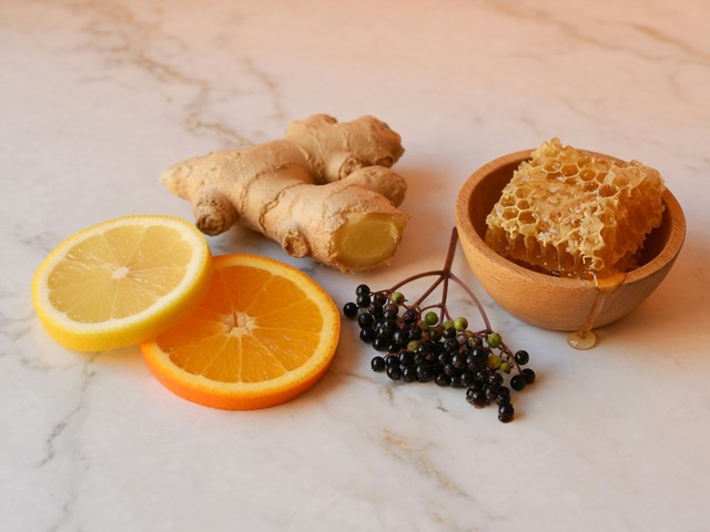 Limone e arancia a fette, radice di zenzero, bacche di sambuco e favo su marmo bianco: motivi dell’elenco degli ingredienti